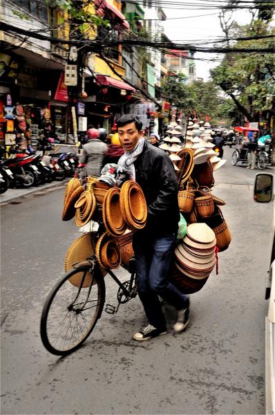 verkoper met hoeden en manden op de fiets in hanoi vietnam.