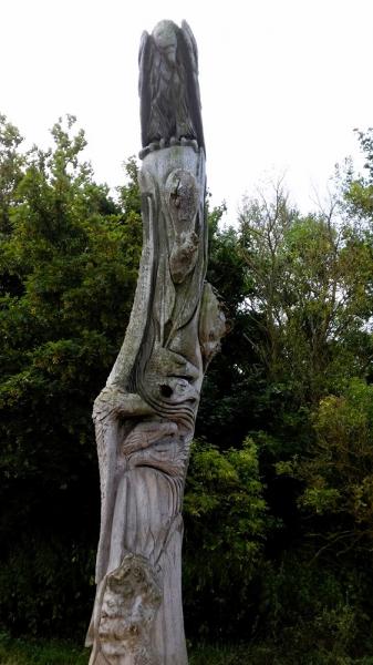 standbeeld havik zit op een bewerkte houten paal / boomstam